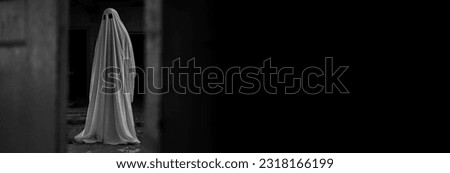 Ghost covered with a white ghost sheet in abandoned house. Image vintage look. Banner. Copy space. Black and white photo