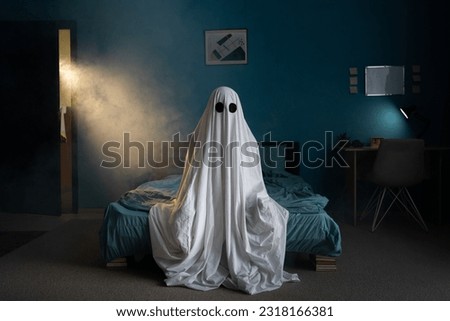 Ghost in a white sheet sits on bed in bedroom, light and smoke on background. Horror scene. Halloween concept. Copy space Royalty-Free Stock Photo #2318166381