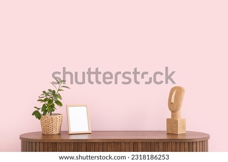 Modern chest of drawers with houseplant and  blank picture near pink wall in room