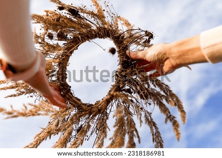 A wreath of a wild meadow flower in the hands of a girl against the sky. Summer solstice day, summer solstice concept, traditional floral decor. pagan witch traditions, wiccan symbols and rituals Royalty-Free Stock Photo #2318186981