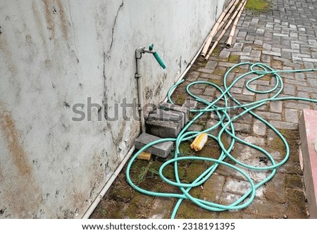 a water tap attached to the wall and there is a hose that is messy on the paving