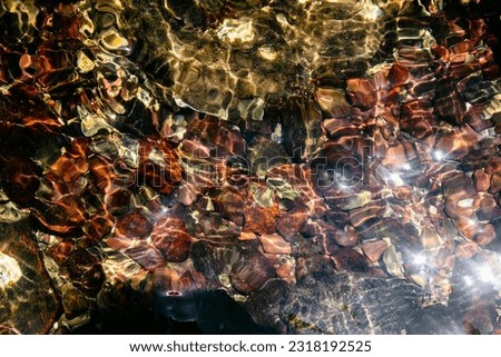 Colorful pebbles on the bottom of the sea water under the sun rays. Beautiful background.
