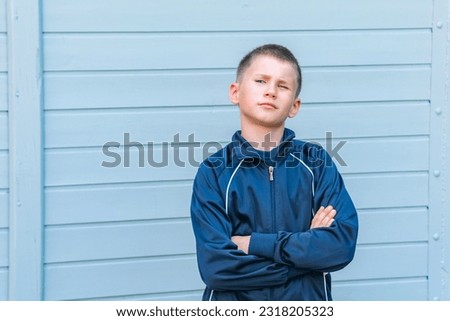 Young adorable teenager squinting his eyes and posing against grey background.
