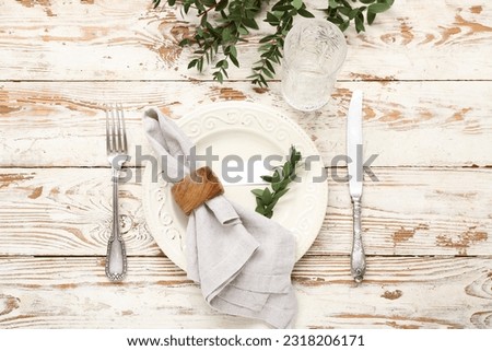 Stylish table setting with blank card and glass on light wooden background