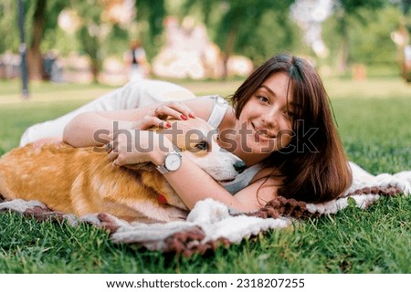 young beautiful girl resting in nature lying on a sheet in the park stroking and kissing small corgi dog animals in nature