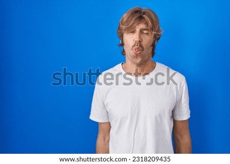 Middle age man standing over blue background making fish face with lips, crazy and comical gesture. funny expression. 