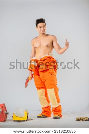 On a white background the firefighter is standing holding an iron axe in one hand giving a thumbs up with a confident smile in the other hand and looking sideways.