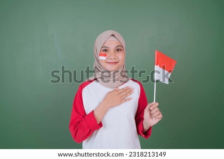 a young asian woman is celebrating Indonesia's independence day with her hands on her chest while waving the red and white flag in front of a green screen