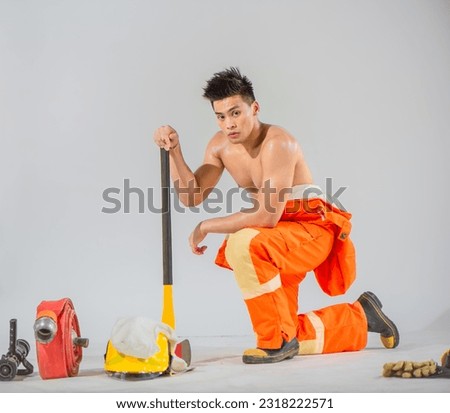 Professional firefighter is kneeling supporting the ground with an iron axe on white background with serious expression.