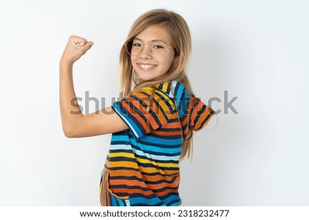 beautiful caucasian teen girl wearing striped sweater over white studio wall,  showing muscles after workout. Health and strength concept. Royalty-Free Stock Photo #2318232477