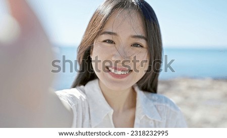 Young chinese woman smiling confident making selfie by the camera at seaside