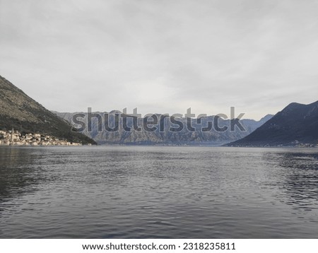 The Bay of Kotor is close to Tivat. Mountains on the right, left and in the background are covered with haze. On the left in the distance are small houses with red roofs. Photo was taken from a yacht.