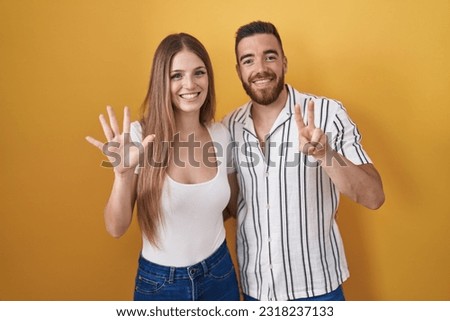 Young couple standing over yellow background showing and pointing up with fingers number seven while smiling confident and happy. 