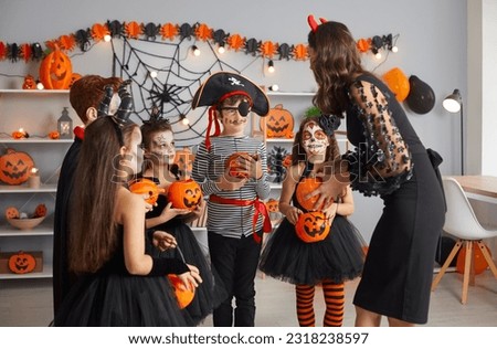 Happy kids in spooky costumes trick or treating at Halloween party. Mom, neighbor or teacher giving candy to group of children dressed up as scary pirates, monsters, witches and vampires