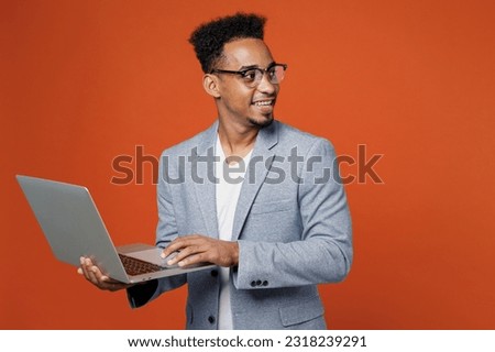 Young employee IT business man corporate lawyer wear classic formal grey suit shirt glasses work in office hold use laptop pc computer look aside on area isolated on plain red orange background studio