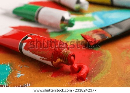 Tube of red oil paint on canvas with abstract painting, closeup