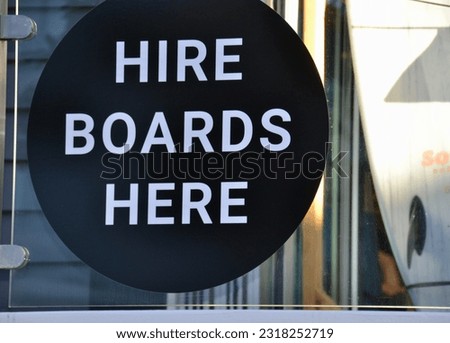 Sign in a surf board rental shop in Noosa, Queensland with equipment in the background suggests boards for hire or rent.