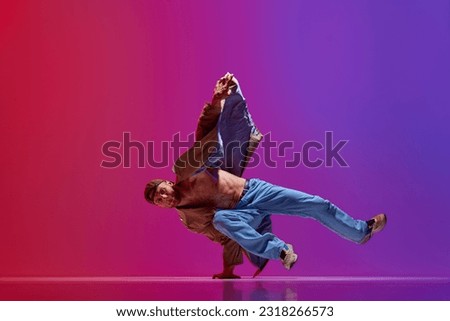 Dance show. Young guy in stylish clothes dancing hip hop, breakdance, contemp against pink purple studio background. Concept of art, street style dance, fashion, youth, hobby, dynamics, ad Royalty-Free Stock Photo #2318266573