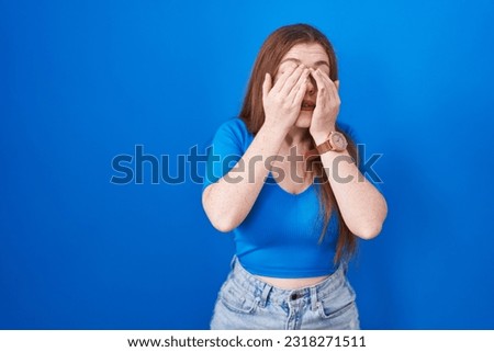 Redhead woman standing over blue background rubbing eyes for fatigue and headache, sleepy and tired expression. vision problem 
