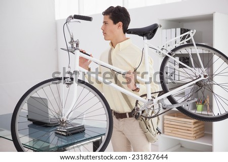 Casual businessman carrying his bicycle in his office