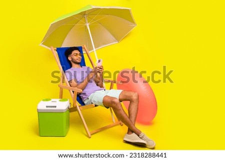 Full length photo of young guy lying sunbed wear shorts read new smartphone messages social media blog isolated on yellow color background
