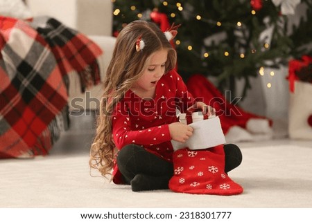 Cute little girl taking gift from Christmas stocking at home
