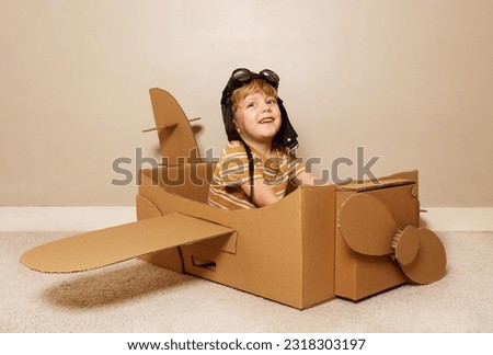 Cute young boy sit in self made cardboard plane with wings and propeller wearing pilot hat, glasses pretend to fly Royalty-Free Stock Photo #2318303197