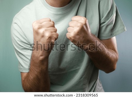 A young handsome man in a fighting stance. Ready to fight. Bare knuckles. Wearing plain shirt. Green and blue background.
