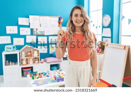 Young caucasian woman working as teacher at kindergarten pointing finger up with successful idea. exited and happy. number one. 