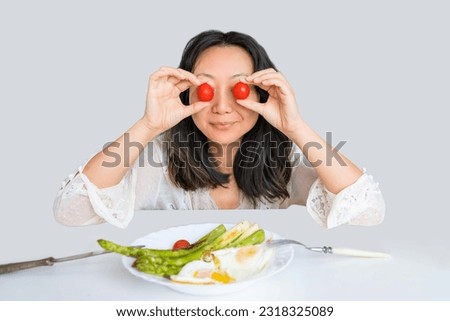 Asian woman eating fried asparagus with eggs and tomatoes isolated. Healthy breakfast.