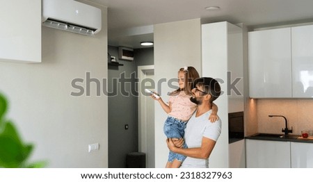 Father kept to hand little girl and turn on air conditioner using remote control. Happy family adjust comfortable temperature of cooler system Royalty-Free Stock Photo #2318327963