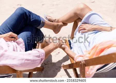 Low section of caucasian senior couple holding hands and sitting on deck chairs at beach. Copy space, unaltered, retirement, vacation, love, together, enjoyment, romance, relaxing nature and summer. Royalty-Free Stock Photo #2318329605