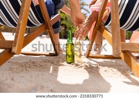 Low section of caucasian senior couple with beer bottles sitting on deck chairs at beach. Unaltered, retirement, vacation, love, together, enjoyment, relaxing, hand, alcohol, nature and summer. Royalty-Free Stock Photo #2318330771