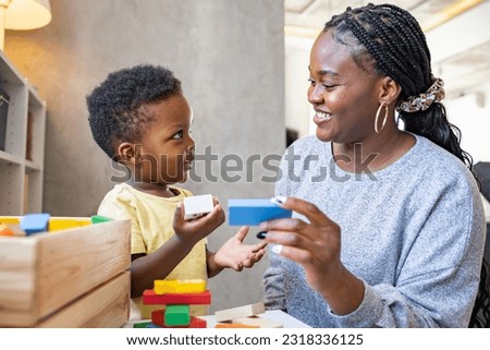 A cute little African child plays with colorful didactic educational toys. His proud mother supports him. Kindergarten teacher with child. Royalty-Free Stock Photo #2318336125