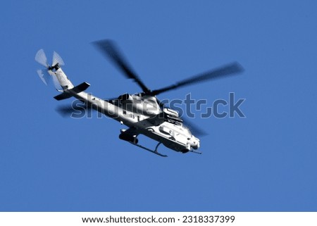 A military attach helicopter in flight in a rich, dark blue sky with the sunlight reflecting off the side of the aircraft. The motion of the rotor blades has been captured in the shot. 