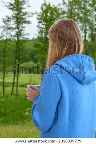 A woman in warm clothes in the middle of the forest, holding a cup of tea