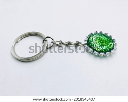 A green colour, circle shape keytag on white background.It has green colour glitter powder, silver keychain and border. It made of resin material. This picture was taken from the side of the keytag.