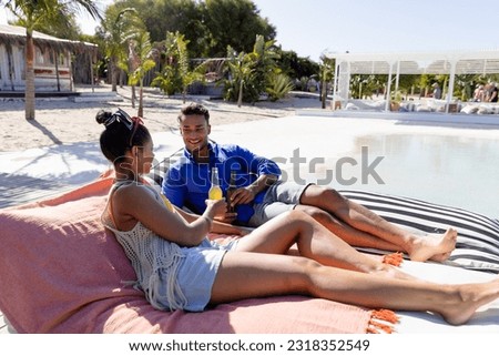 Happy caucasian young couple toasting beer bottles while relaxing on loungers at tourist resort. Copy space, unaltered, vacation, love, together, lifestyle, enjoyment, beach, alcohol and summer.
