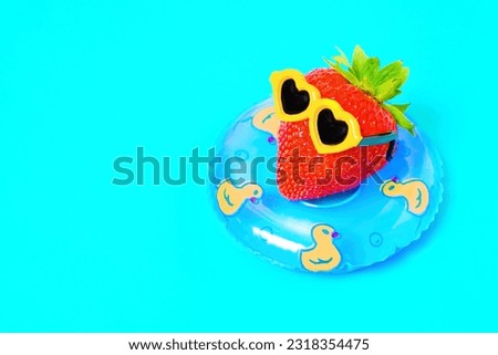 Juicy strawberry, adorned with stylish sunglasses, indulges in a relaxing sunbathing session as it floats gracefully in a pool ring. Summer retreat concept.