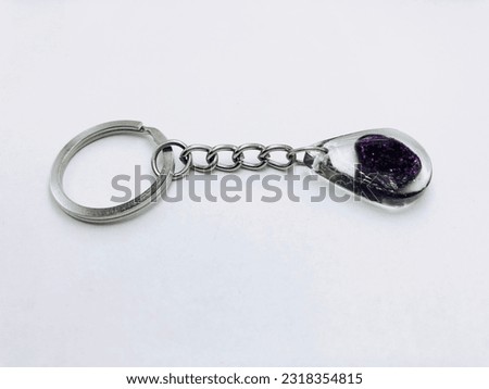 A black colour,water drop shape keytag on white background.It has black heart and inside purple glitter, silver keychain.It made of resin material.This picture was taken from the side of the keytag.