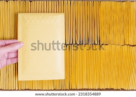 Hand holds one yellow padded envelop from the delivered batch. Acceptance and quality control. Royalty-Free Stock Photo #2318354889