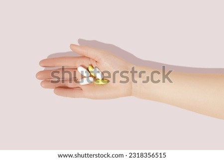 Female hand holding pills on pink background