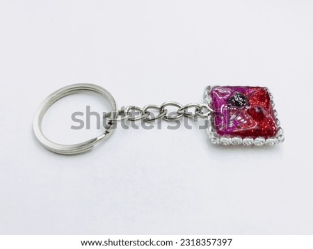 A red and pink colour, square shape keytag on white background.It has red and pink glitter powder,silver keychain,border.It made of resin material.This picture was taken from the side of the keytag.