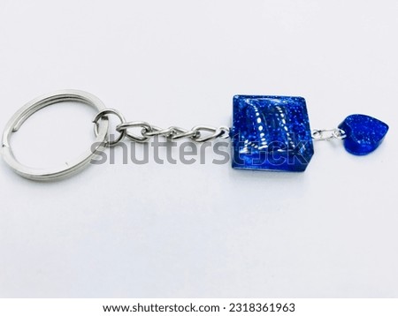 A blue colour, square and heart shape keytag on white background.It has blue glitter powder , silver keychain.It made of resin material.This picture was taken from the side of the keytag.Beautiful.