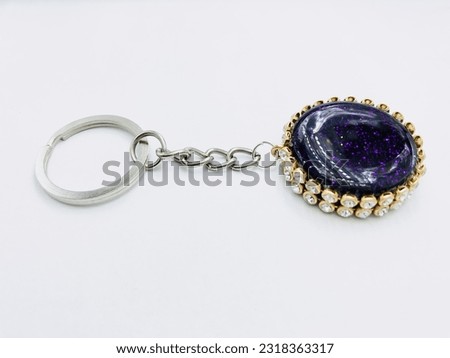 A black colour, circle shape keytag on white background.It has purple glitter powder,silver keychain,gold border.It made of resin material.This picture was taken from the side of the keytag.Beautiful.