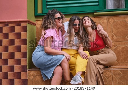 Three seated friends pose laughing and hugging in fun attitude.