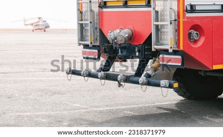 Airfield fire engine from behind. Special bumper equipment for extinguishing fuel spills and creating foam strips during emergency landings of aircraft. The helicopter is blurred in the background.