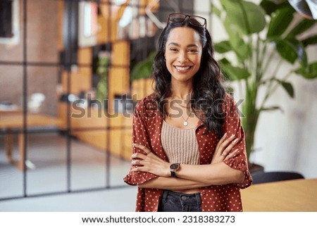 Portrait of smiling young multiethnic woman looking at camera with crossed arms. Successful latin business woman standing in modern office with copy space. Young university hispanic girl with smile. Royalty-Free Stock Photo #2318383273