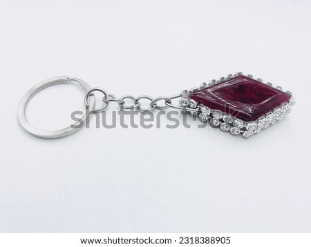 A dark red colour, rhombus shape keytag on white background.It has silver keychain and border. It made of resin material. This picture was taken from the side of the keytag. Beautiful creative keytag.