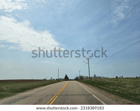 An open rural road with farm land on either side of it.